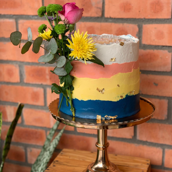 Bolo em camadas de cores com flores frescas sobre suporte dourado